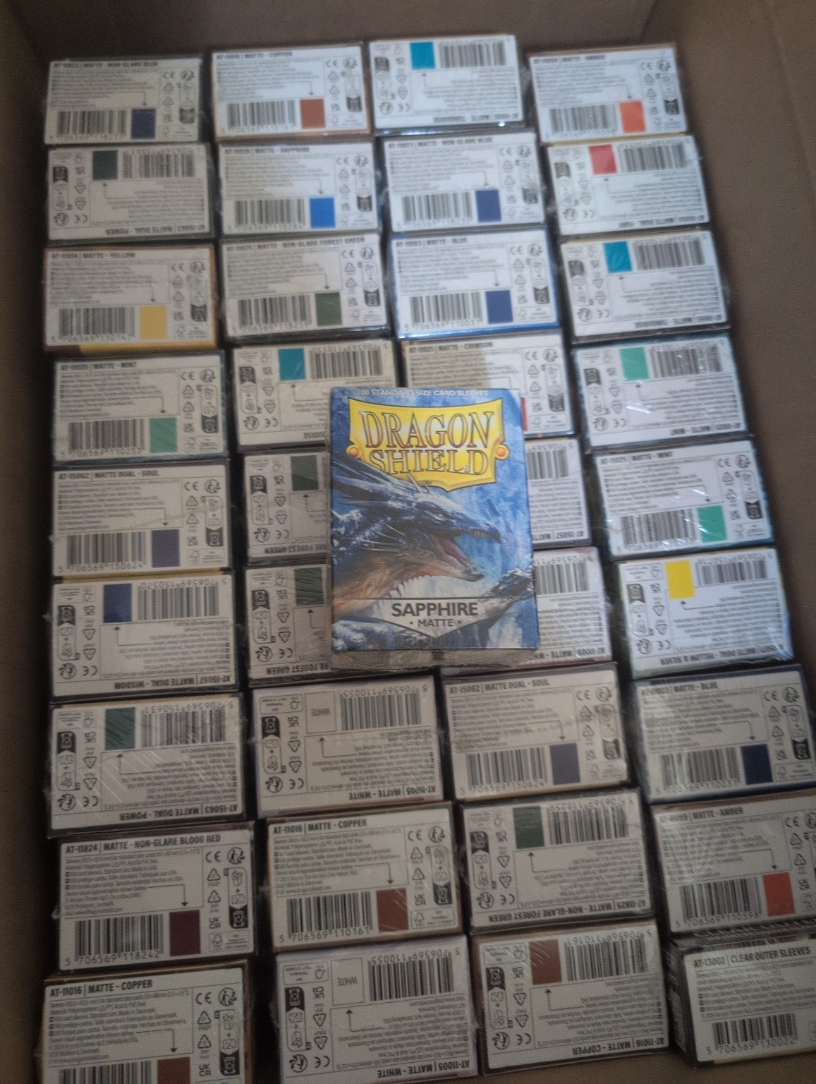 Boxes of Dragon Shield standard and Japanese-size card sleeves in multiple colors